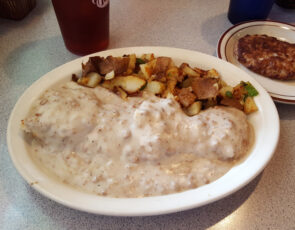 Biscuits and gravy on plate, potatoes and sausage.