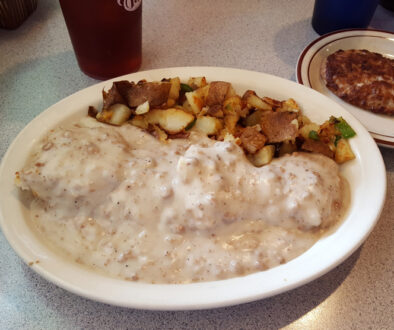 Biscuits and gravy on plate, potatoes and sausage.