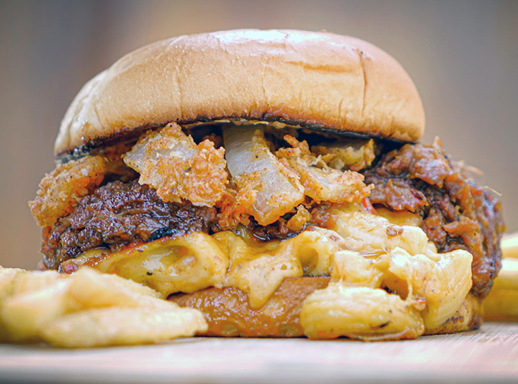 The Fat Guys Pork and Mac Stack combines all your favorites into one OMG burger: BBQ pulled pork and a Mac & Cheese patty, on toasted bun, topped with the Fat Guys Grill’s signature onion fries. Photo: Jesse Harding.
